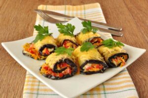 involtini di melanzane su un piatto e dietro forchetta e coltello