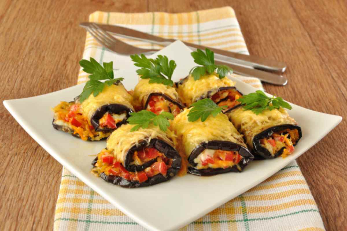 involtini di melanzane su un piatto e dietro forchetta e coltello
