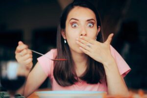 ragazza che si porta la mano davanti la bocca mentre mangia