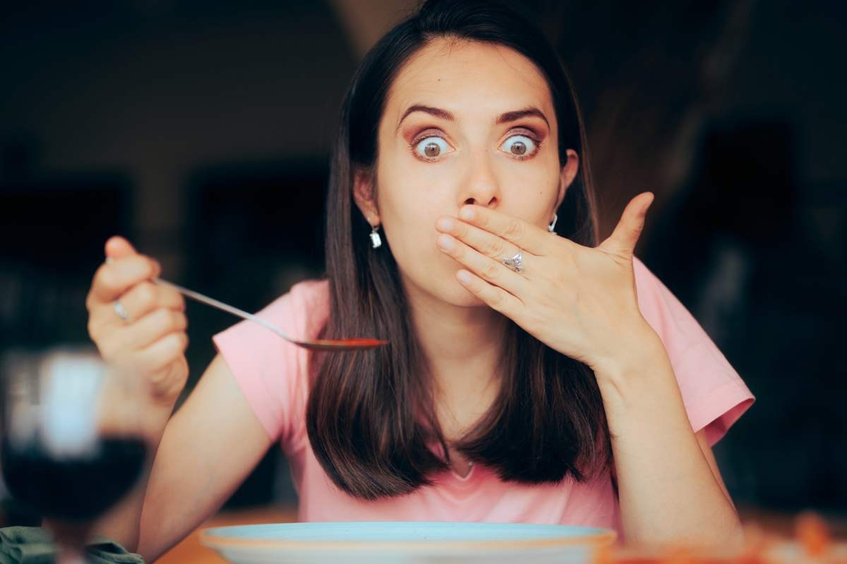 ragazza che si porta la mano davanti la bocca mentre mangia