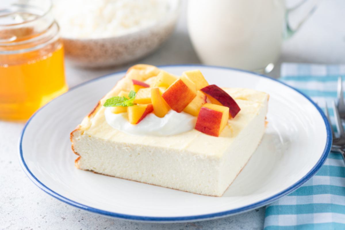 fetta di torta allo yogurt sopra ad un piatto con sopra delle pesche a cubetti