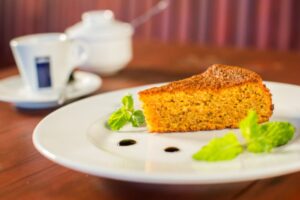 fetta di torta alle carote su un piatto e dietro una tazzina di caffè